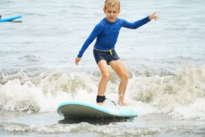 Boy in a blue rash guard riding a wave on a blue surfboard, Summer Surfkid Camp Hong Kong