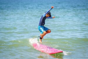 Kid jumping off a pink surfboard into the sea, Summer Surfkid Camp at Lower Cheung Sha Beach