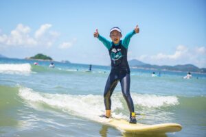 Girl giving a thumbs up while surfing a wave, Summer Surfkid Camp at Lower Cheung Sha