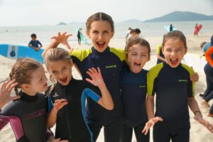 Group of Surfkids Camp kids in wetsuits cheering on Lower Cheung Sha Beach, Easter Surfkid Camp