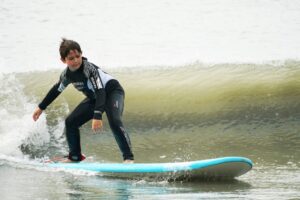 Boy in a wetsuit riding a small wave on a blue surfboard, Easter Surfkid Camp Hong Kong