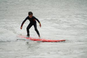 Kid in a wetsuit riding a red surfboard toward the shore, Easter Surfkid Camp Hong Kong