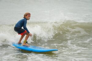 Kid in a wetsuit surfing a blue board on a winter wave, Winter Surfkid Camp at Lower Cheung Sha