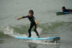 Boy in a wetsuit balancing on a blue surfboard, Winter Surfkid Camp at Lower Cheung Sha