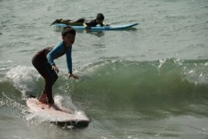 Young surfer in a wetsuit riding a wave on a red board, Winter Surfkid Camp Hong Kong