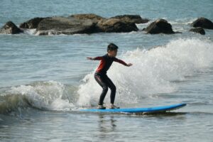 Boy in a wetsuit surfing near the rocks at Lower Cheung Sha Beach, Winter Surfkid Camp