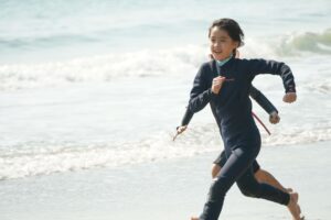 Girl in a wetsuit running through the shallows, Winter Surfkid Camp Hong Kong