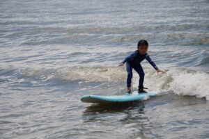 Boy in a rash guard surfing a small wave on a blue board, Autumn Surfkid Camp Hong Kong