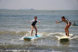 Two kids riding waves side by side on surfboards, Autumn Surfkid Camp Hong Kong