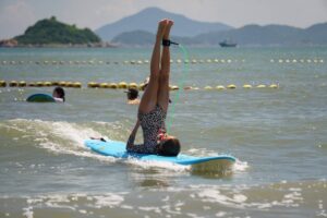Girl doing a handstand on a surfboard in the sea, Autumn Surfkid Camp at Lower Cheung Sha Beach