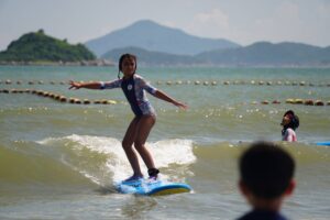 Girl with her arms out surfing toward the beach, Autumn Surfkid Camp Hong Kong