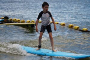 Boy standing on a blue surfboard beside the swim-zone buoys, Autumn Surfkid Camp at Lower Cheung Sha