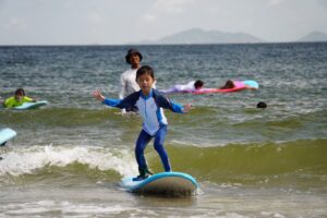Boy in a blue rash guard surfing with his arms out, Autumn Surfkid Camp Hong Kong