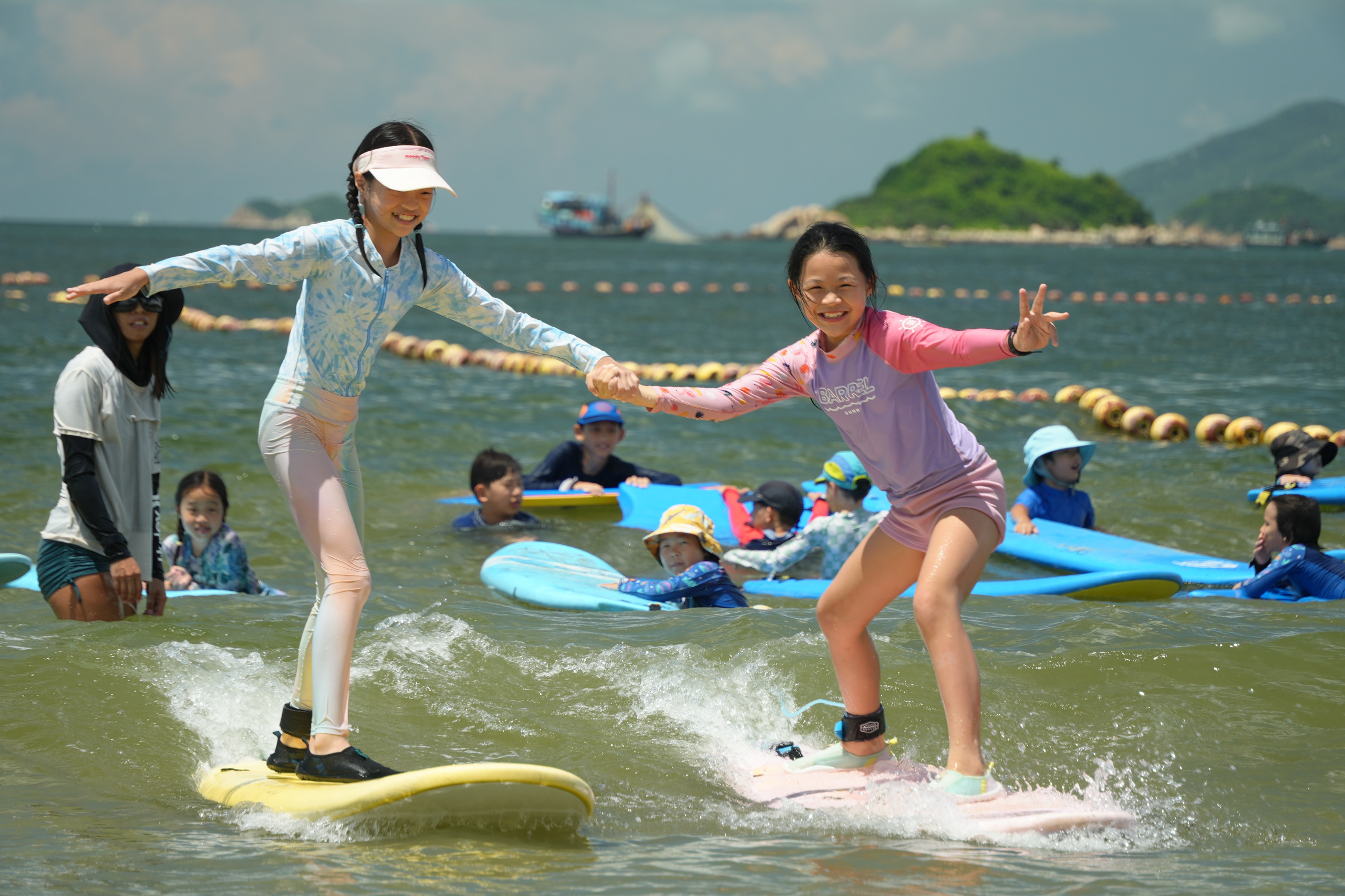 Two girls standing on surfboards beside a coach at Lower Cheung Sha Beach, Hong Kong Surfkids Camp